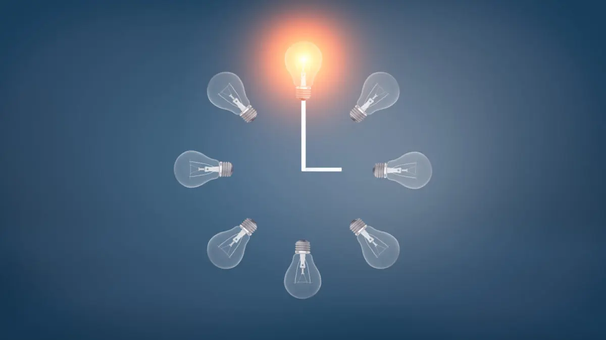 3d rendering of a several incandescent light bulbs arranged in the clock shape with one glowing bulb on the top.