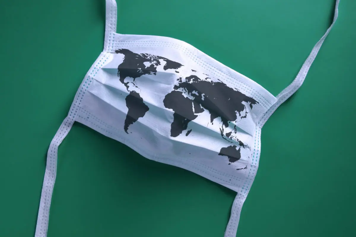White face mask with a map of the world is lying on a green background