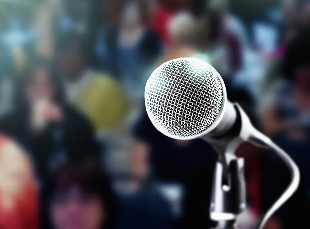 Brightly lit microphone with dark, defocused audience in the background