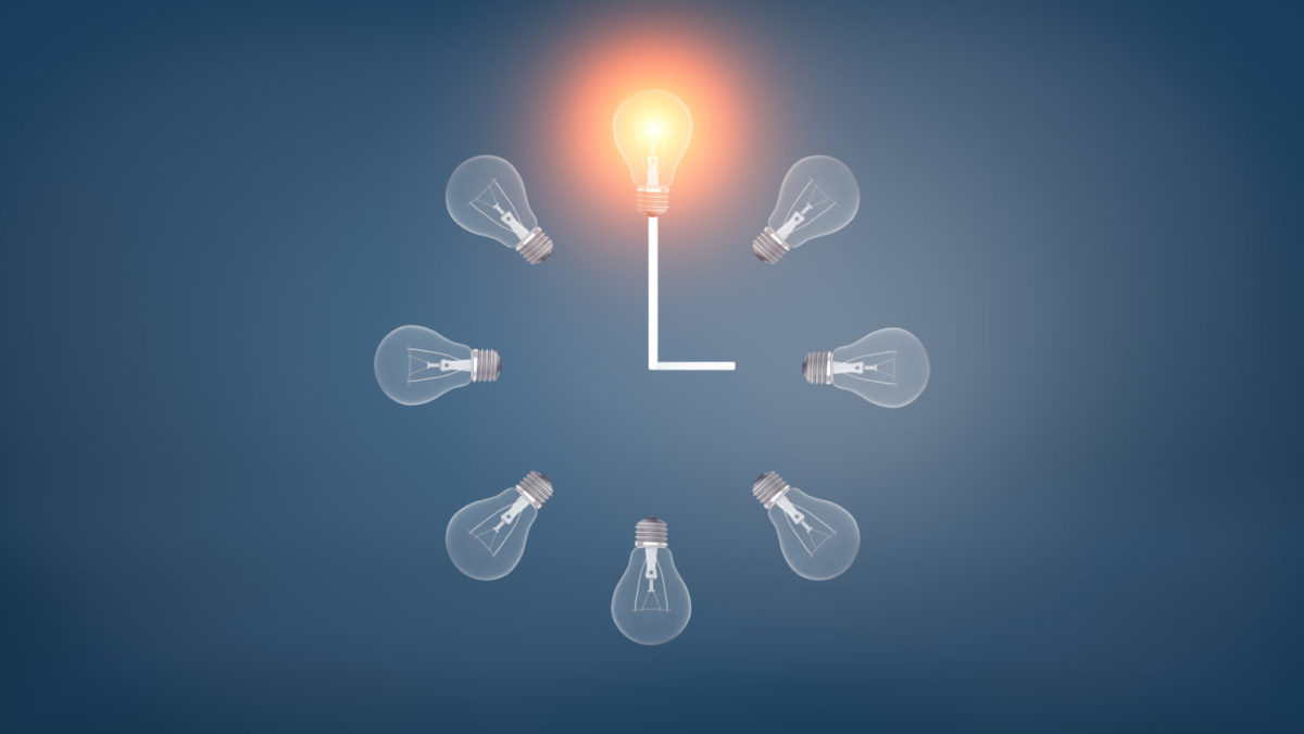 3d rendering of a several incandescent light bulbs arranged in the clock shape with one glowing bulb on the top.